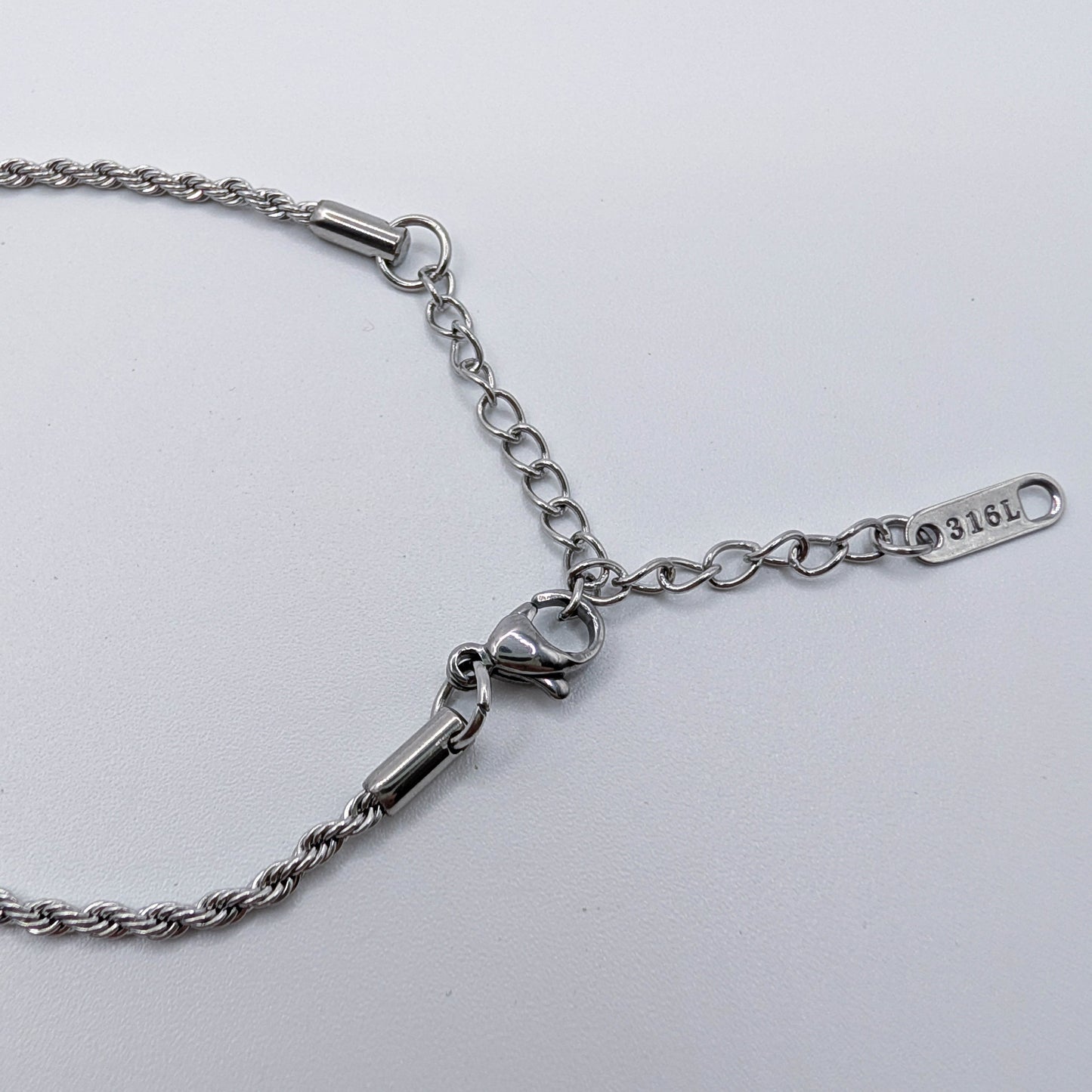 Close up of silver stainless steel bracelet on a light gray background, showing the 316L label.