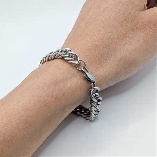 A close-up of a person's wrist wearing a chunky silver-toned chain bracelet with a lobster clasp, photographed against a plain light background.