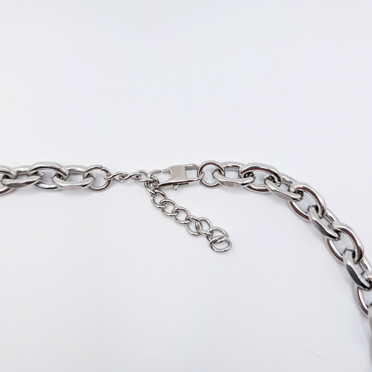 Close-up of a silver stainless steel metal chain necklace with a lobster clasp and extender chain on a plain light background.