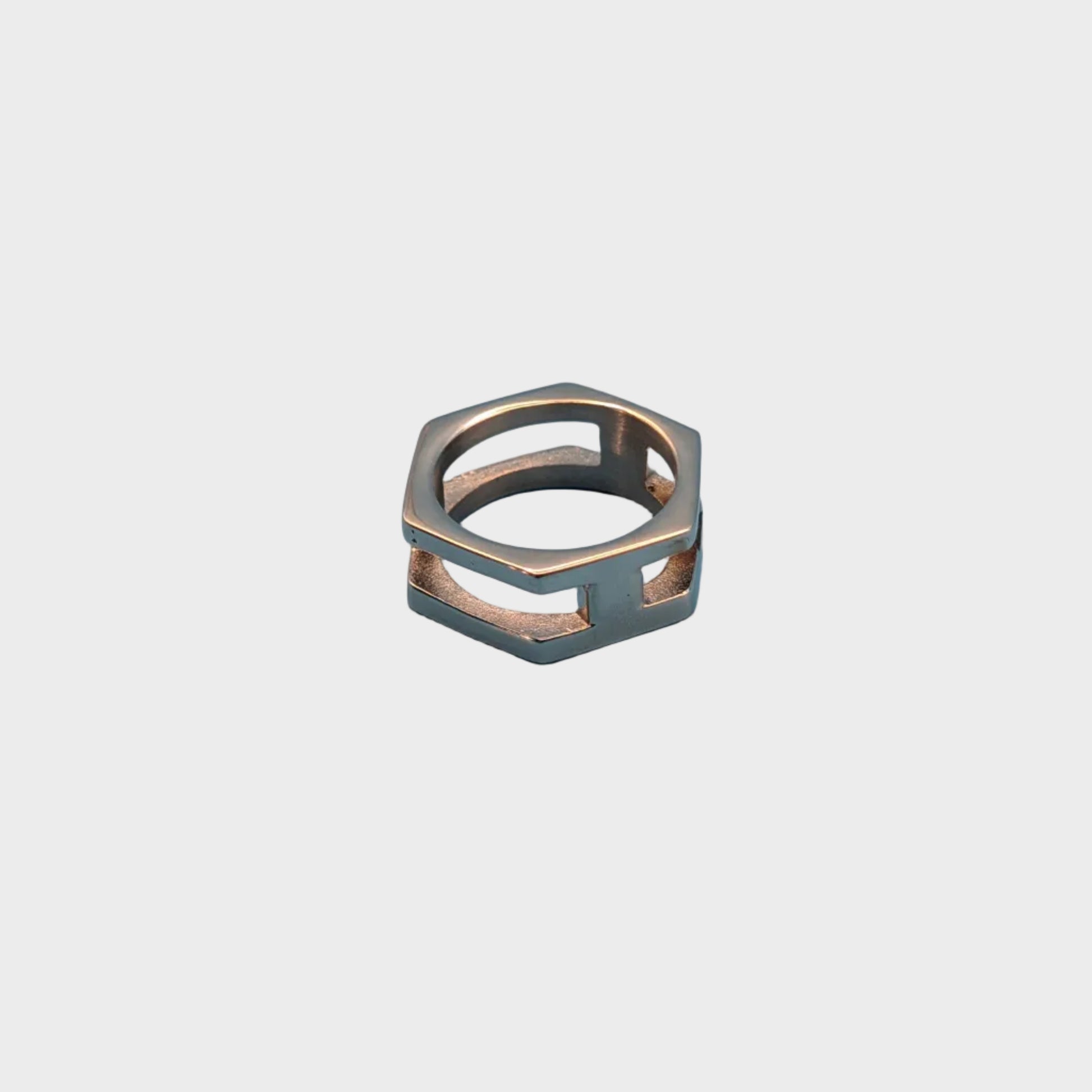 A geometric hexagonal ring with a dual-tone metallic finish, featuring a silver-toned outer frame and a rose gold-toned inner band, set against a solid light blue background.