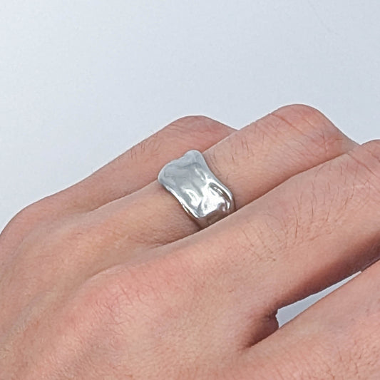 Stainless steel ring on a person's finger against a light gray background