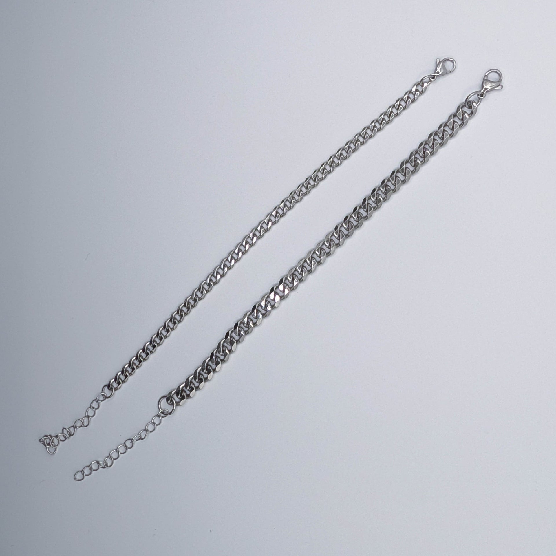 Two variants of the stainless steel cuban link style chain bracelet on a light gray background.
