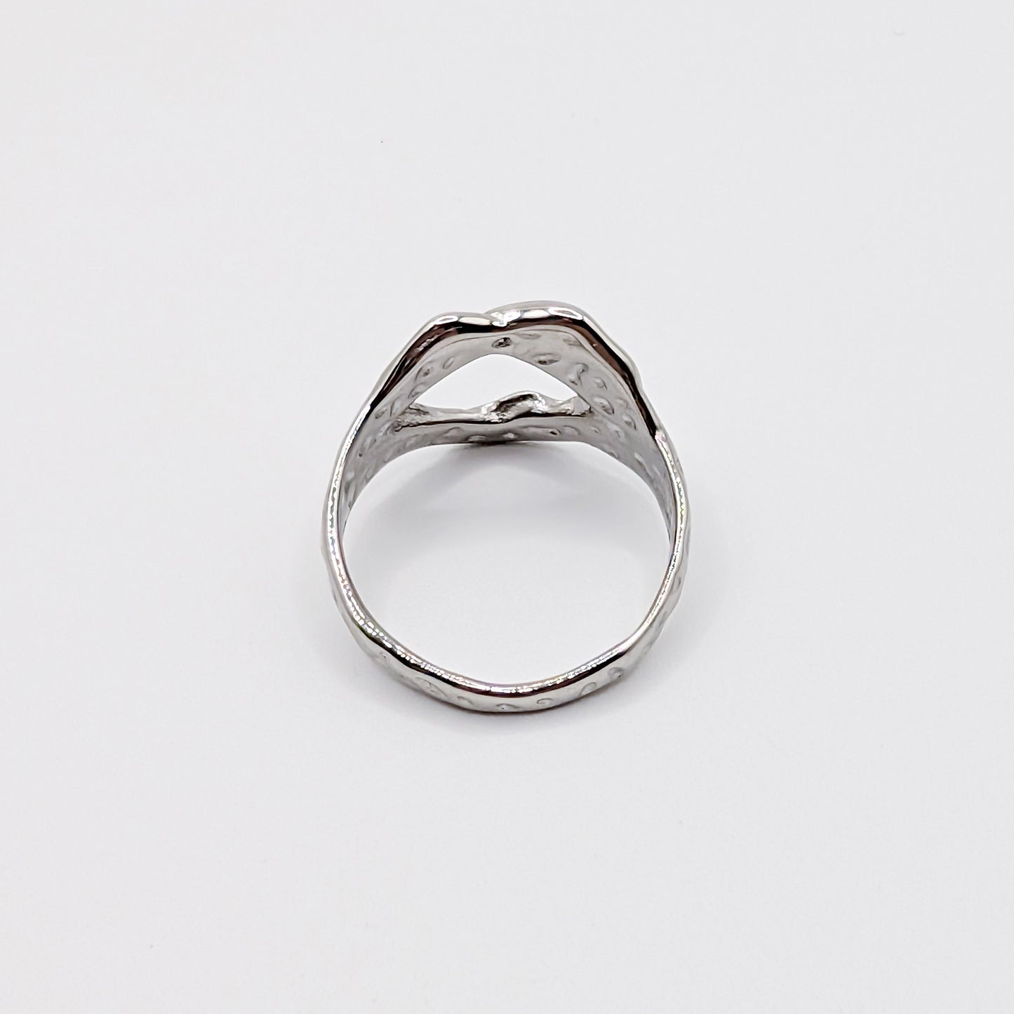 Alternative angle of textured stainless steel ring with an open cutouts on a white background.