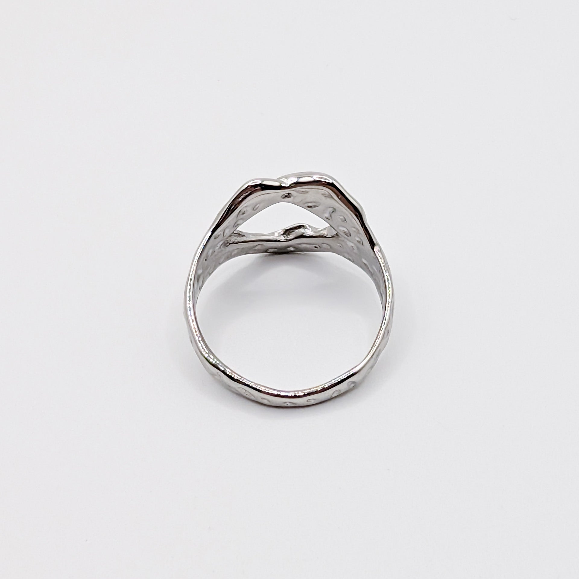 Alternative angle of textured stainless steel ring with an open cutouts on a white background.