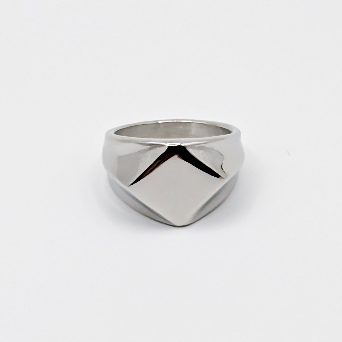Polished minimalist stainless steel signet ring with a geometric diamond shaped pointed face on a clean white background.