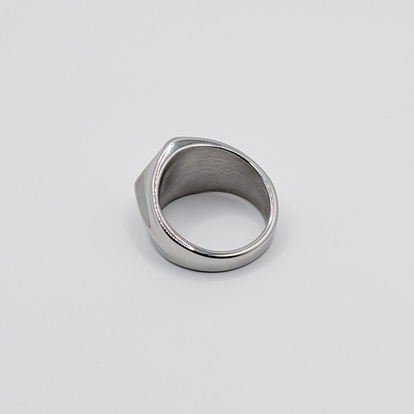 Back view of polished minimalist stainless steel signet ring with a geometric diamond shaped pointed face on a clean white background.