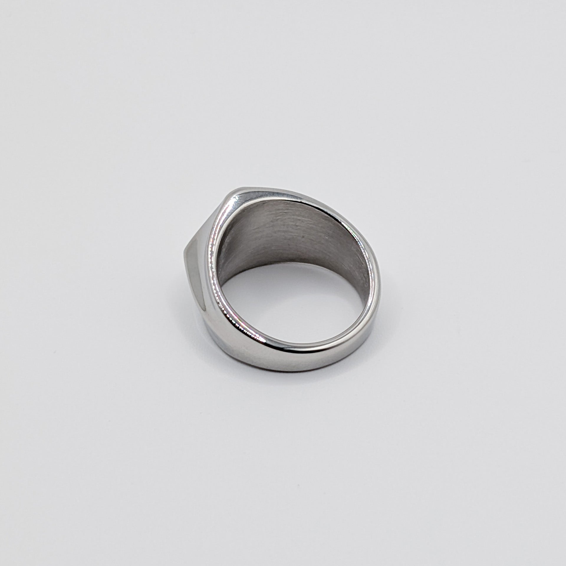 Back view of polished minimalist stainless steel signet ring with a geometric diamond shaped pointed face on a clean white background.