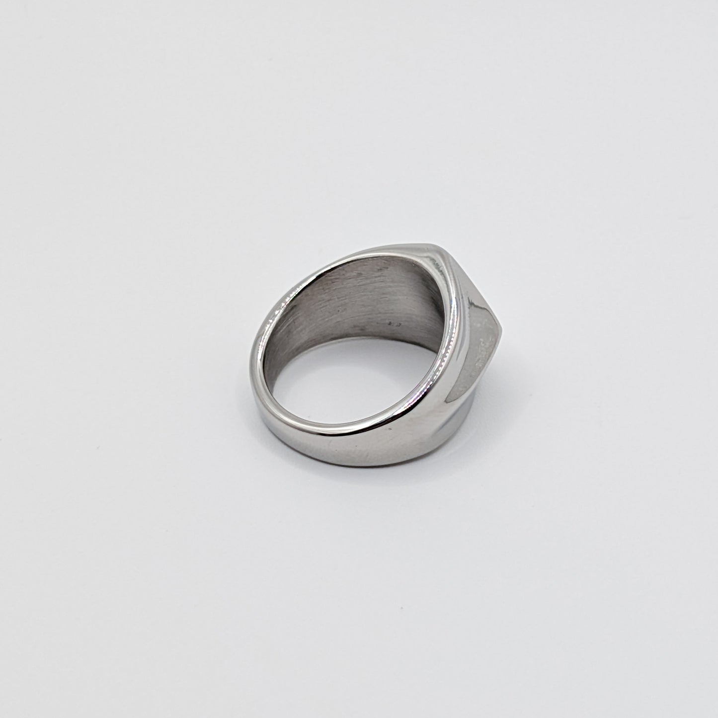 Side view of polished minimalist stainless steel signet ring with a geometric diamond shaped pointed face on a clean white background 