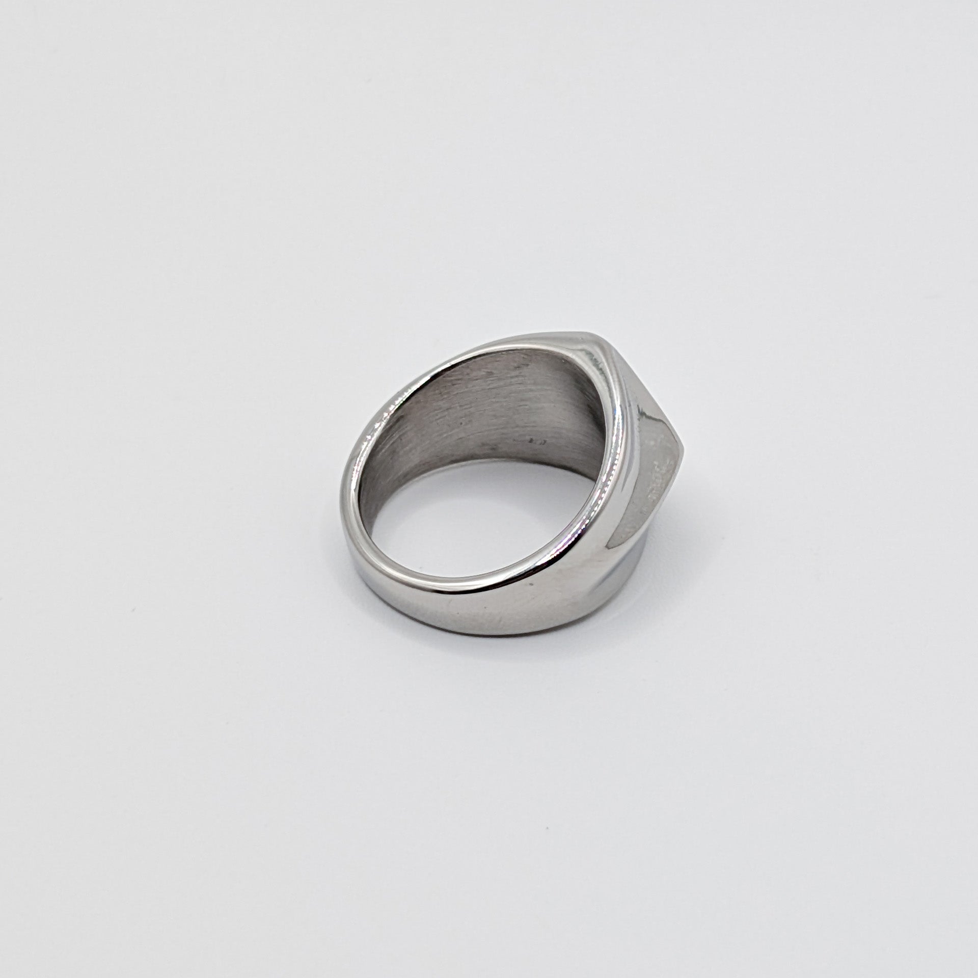 Side view of polished minimalist stainless steel signet ring with a geometric diamond shaped pointed face on a clean white background 