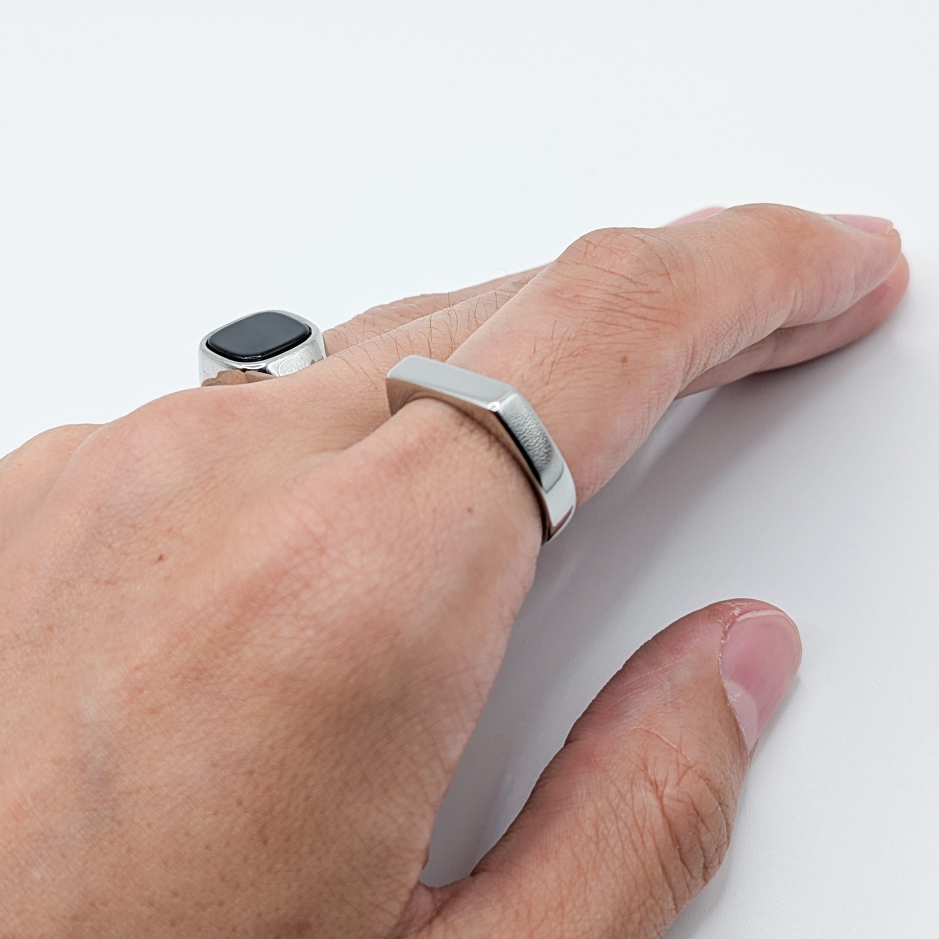 Close-up of a thick silver minimalist block ring worn on a model's finger, styled with stainless steel ring with black stone.