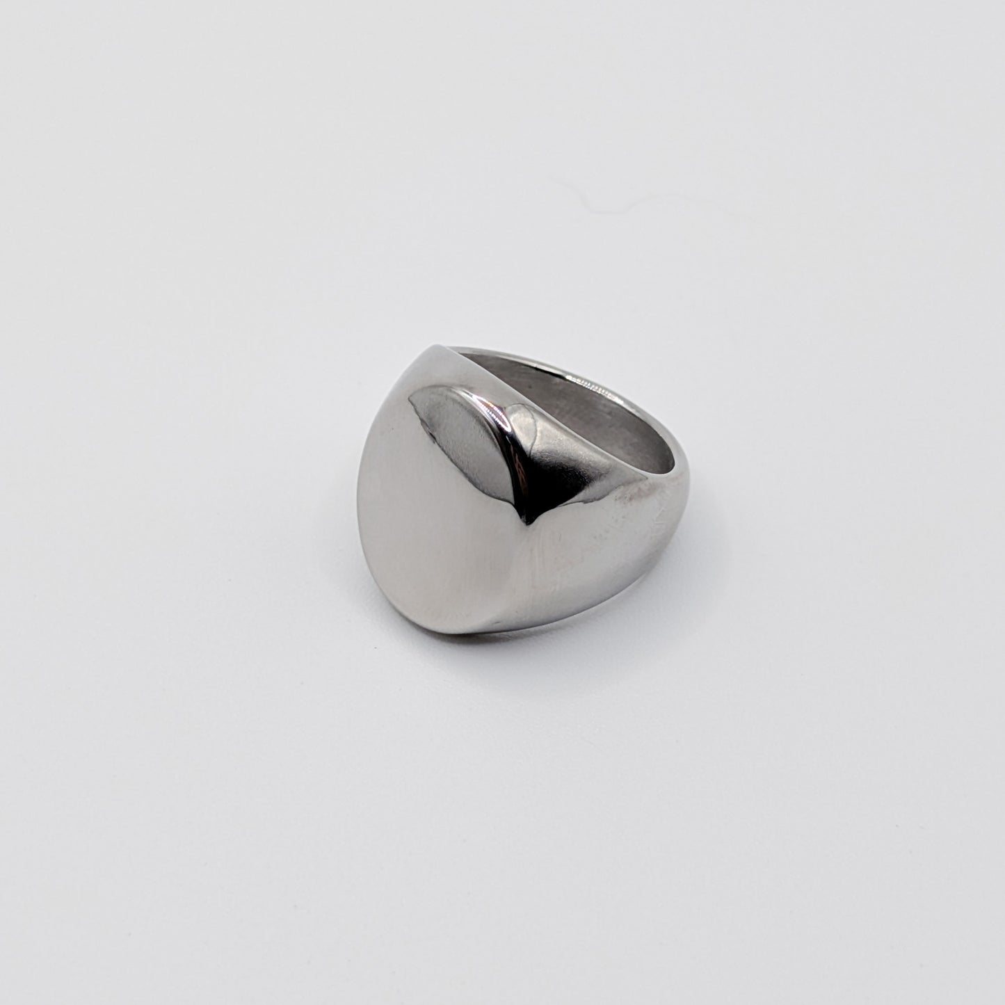 Side view of thick polished minimalist stainless steel signet ring on a white background.