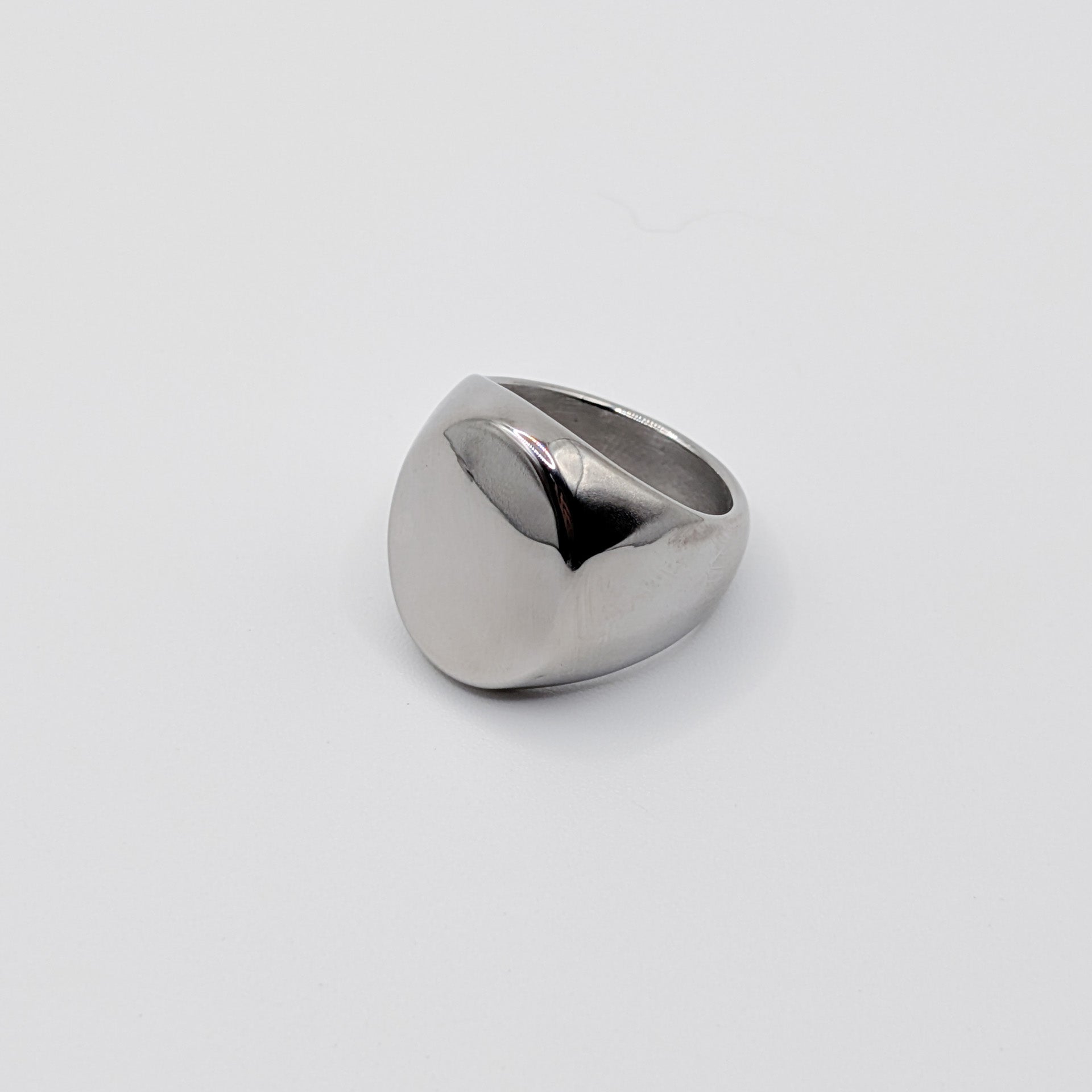 Side view of thick polished minimalist stainless steel signet ring on a white background.