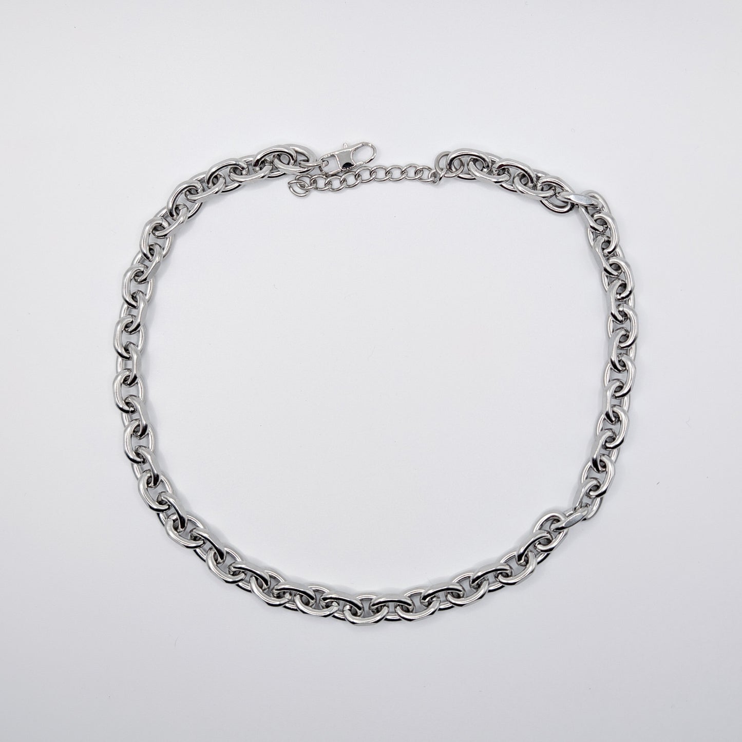 A stainless steel cable chain necklace with a lobster clasp, arranged in a circle on a plain light gray background.
