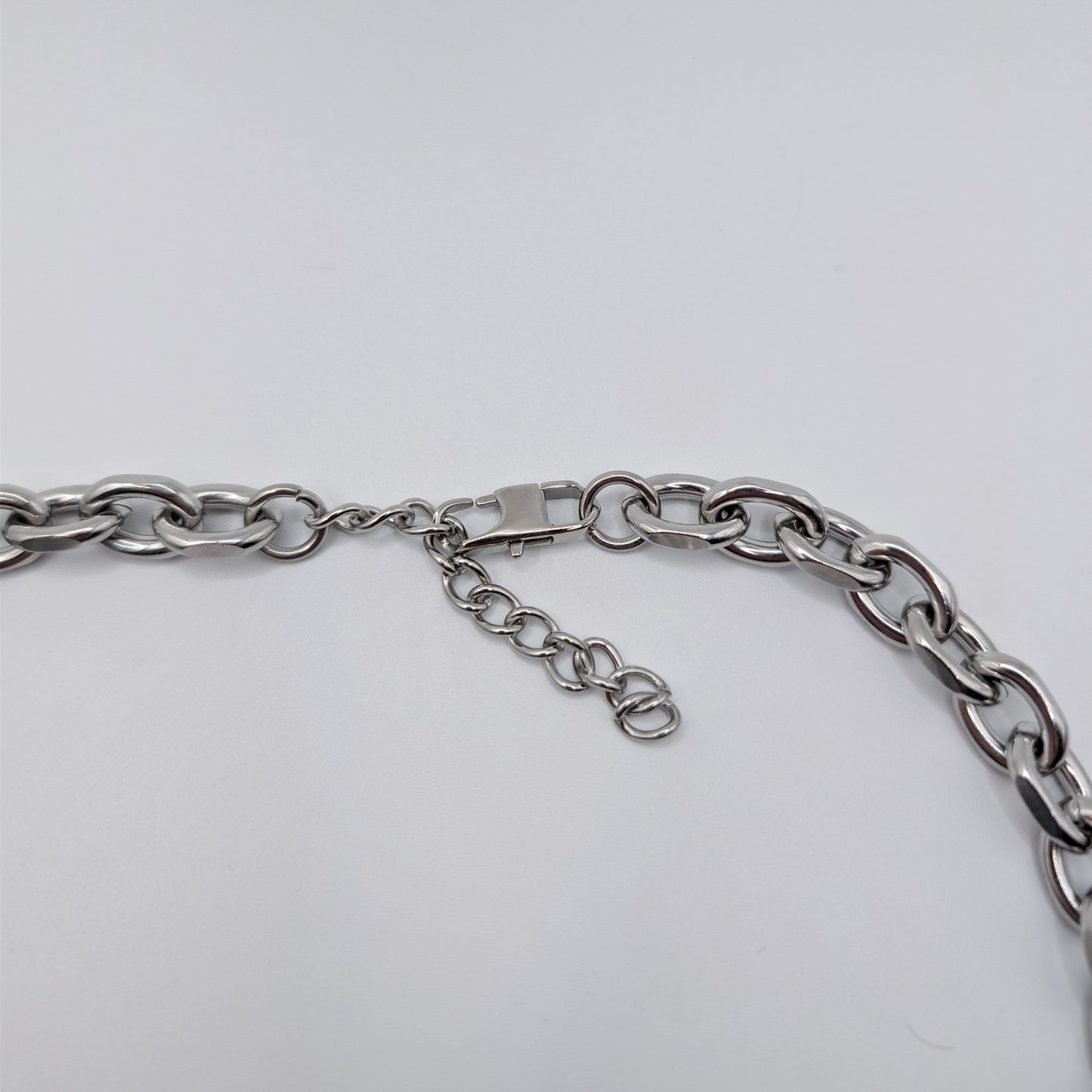 Close-up of a silver stainless steel metal chain necklace with a lobster clasp and extender chain on a plain light background.