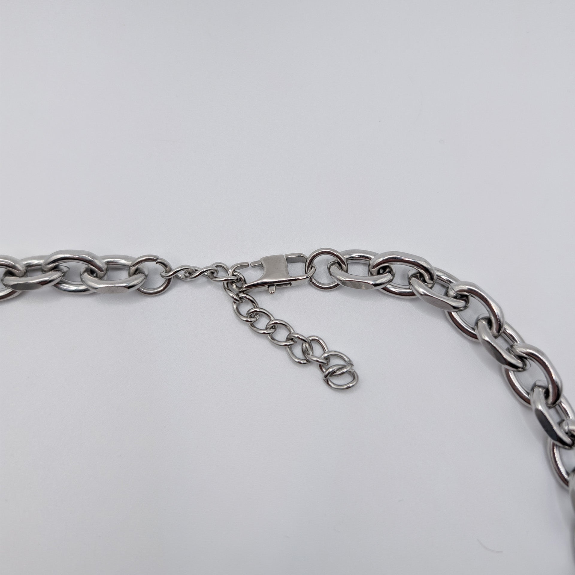 Close-up of a silver stainless steel metal chain necklace with a lobster clasp and extender chain on a plain light background.