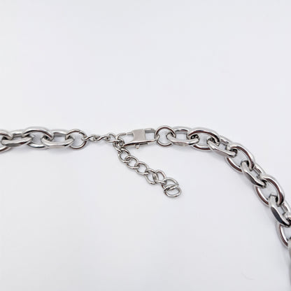 Close-up of a silver stainless steel metal chain necklace with a lobster clasp and extender chain on a plain light background.