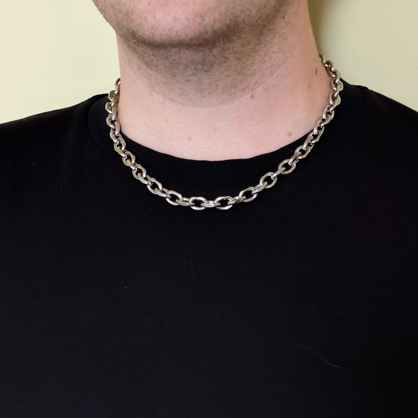 Close up of the stainless steel cable chain necklace with a lobster clasp, on a model with black shirt.